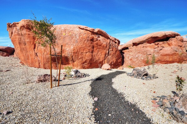 A desert landscape with large red rock formations and a gravel path leading towards them.