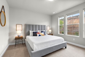 A bedroom with a large bed, two bedside tables, a headboard, and a window with a view of a rocky landscape.