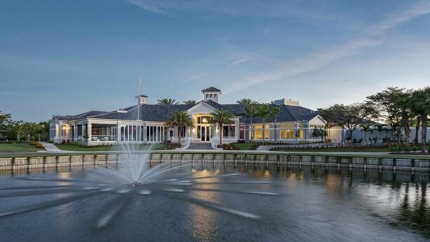 A large, elegant building with a fountain in front, surrounded by palm trees and a well-maintained lawn. - Luxurious golf home with pool in prestigious Colonial Country Club + Amenities (Fort Myers)