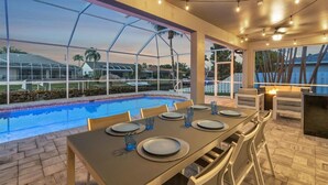 An outdoor dining area with a pool view, a covered patio, and string lights. - OCEANLUX-Luxury+Gulf_Access+Heated_Pool+Kayaks+Golf+Chefs_Kitchen+Games (Cape Coral)