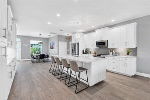 Una cocina moderna con armarios blancos, una isla grande con taburetes y una zona de comedor con mesa y sillas.