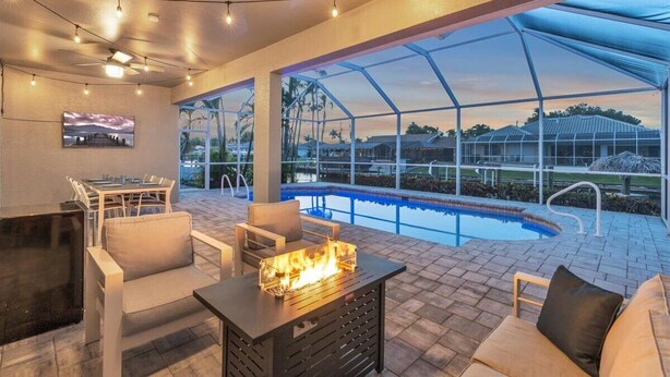 An outdoor pool area with a fire feature, seating, and a view of a residential area. - OCEANLUX-Luxury+Gulf_Access+Heated_Pool+Kayaks+Golf+Chefs_Kitchen+Games (Cape Coral)