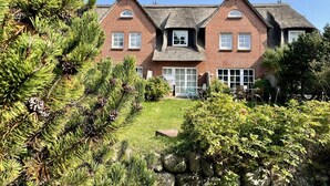A large brick house with a thatched roof, a front porch, and a well-maintained garden with pine trees and shrubs. - Haus Shelly - 3-zimmer Haus für 5 Personen: Terrasse, 2 Stellplätzen, Wlan. Haustier Erlaubt (Sylt-Ost)