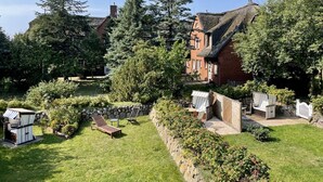 A traditional house with a thatched roof, surrounded by a well-maintained garden with a lawn, a wooden deck, and a stone wall. - Haus Shelly - 3-zimmer Haus für 5 Personen: Terrasse, 2 Stellplätzen, Wlan. Haustier Erlaubt (Sylt-Ost)