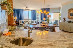 A modern kitchen with a marble countertop, stainless steel sink, and a dining area with a table and chairs. - Sand Dunes 1232 (Myrtle Beach)