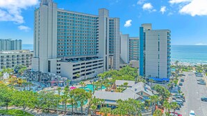 Un hotel moderno de gran altura con varios pisos, un garaje y una zona de piscina con palmeras.
