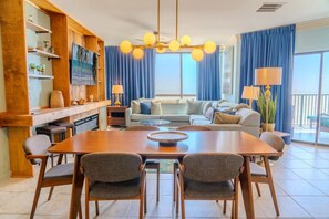 A dining area with a wooden table, four chairs, a sofa, and a TV on a wooden shelf.