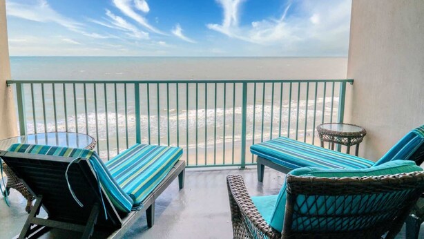 Un balcón con vistas a la playa, dos sillones de descanso, una mesita y una silla de mimbre.