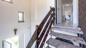 Eine Treppe mit Holzboden und Metallgeländern, die zu einem Flur führt, von dem aus man eine Küche und einen Essbereich sieht.