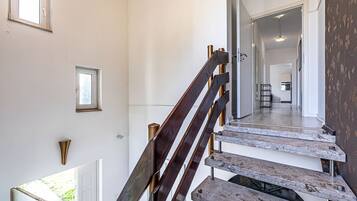 Eine Treppe mit Holzboden und Metallgeländern, die zu einem Flur führt, von dem aus man eine Küche und einen Essbereich sieht.