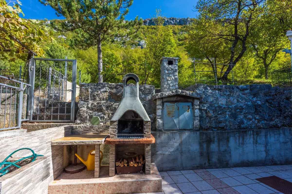 A stone wall, a metal gate, and a small outdoor grill area with a chimney.