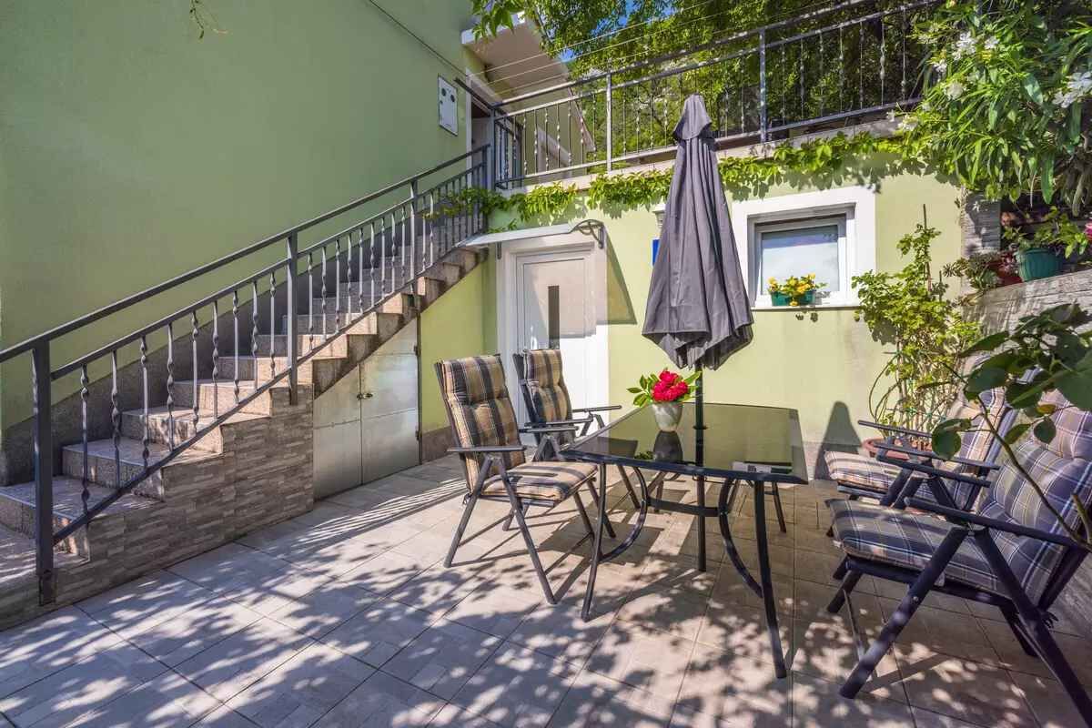 Une terrasse avec une table et des chaises, un escalier et une fenêtre ornée de plantes.