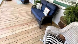 Une véranda couverte avec des meubles en osier, un canapé bleu et une chaise blanche.