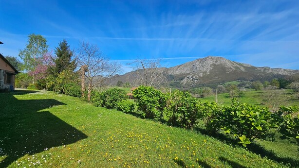 A grassy area with a mountain in the background, a building on the left, and a clear sky.