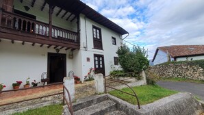 A two-story white building with a balcony, a stone wall, and a paved entrance area with steps.