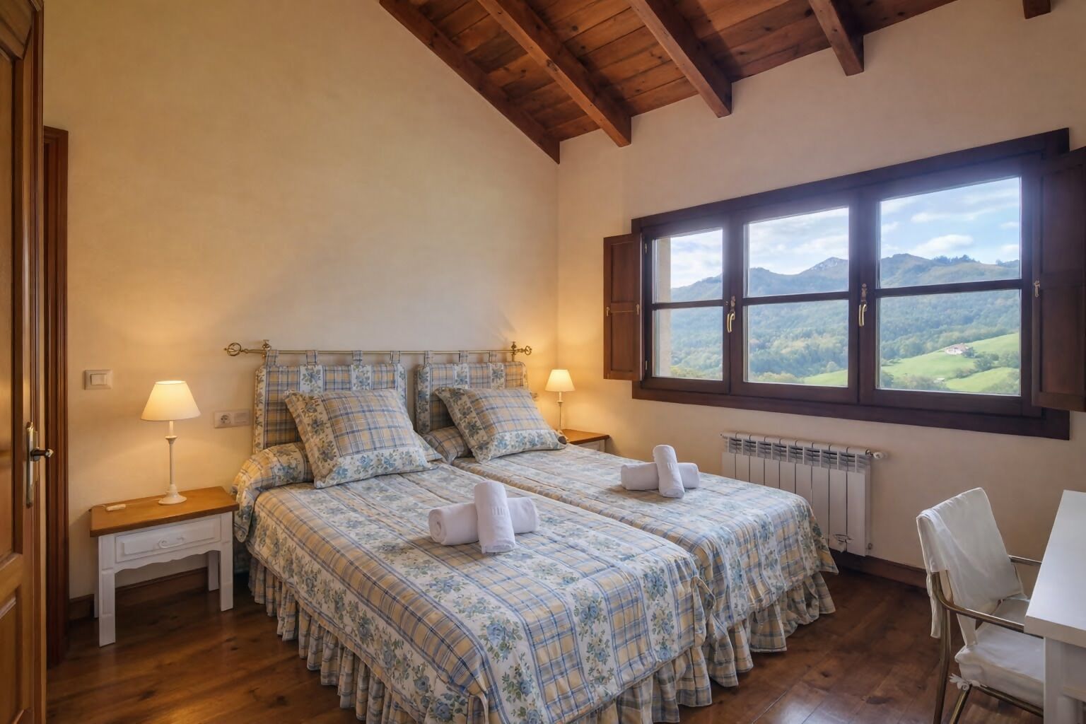 Ein Schlafzimmer mit zwei Betten, einem Fenster mit Bergblick, Holzbalken an der Decke und einer Heizung.