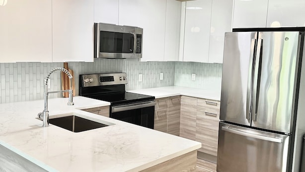 Una cucina moderna con mobili bianchi, un frigorifero in acciaio inossidabile, un forno a microonde e un lavello con un rubinetto dal design moderno.