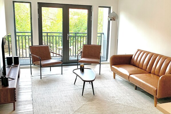 A living room with a brown leather sofa, two brown armchairs, a small coffee table, and a TV on a wooden stand. - Luxury apartment in the heart of Quincy (Quincy)