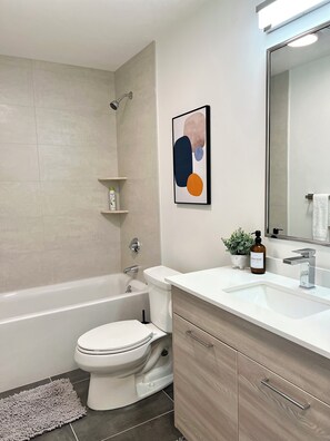 A modern bathroom with a bathtub, toilet, and sink. There is a framed abstract artwork on the wall and a small potted plant on the sink counter. - Luxury apartment in the heart of Quincy (Quincy)