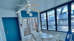 Une pièce avec une porte bleue, une fenêtre grillagée, une table ronde entourée de chaises et un ventilateur de plafond.