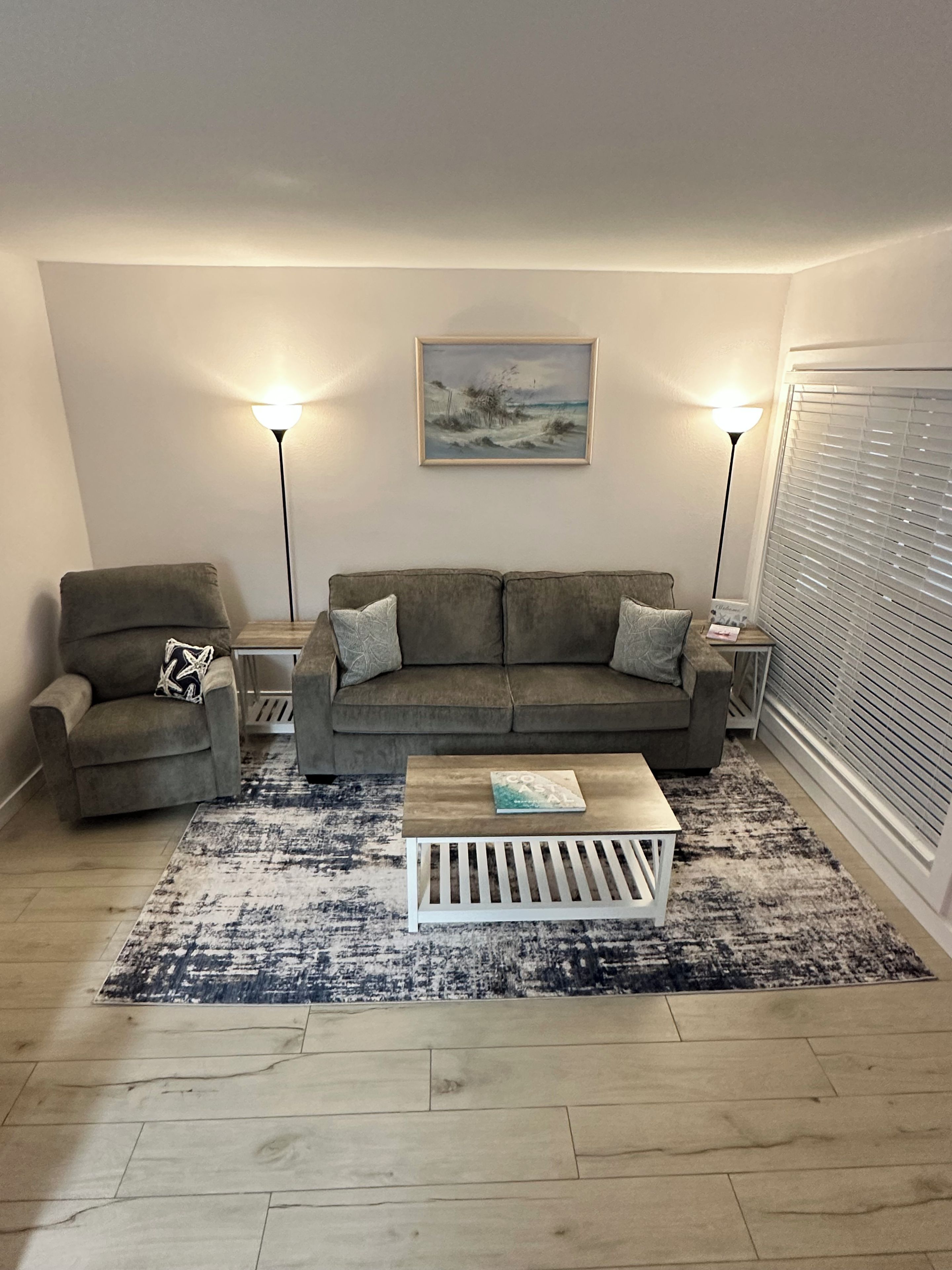 Un salon avec un canapé gris, un fauteuil plus petit, une table basse et deux lampadaires.