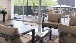 A spacious balcony with wicker furniture, large windows, and a view of a forested area. - Fight Club Philippines (Puerto Princesa)