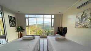 A hotel room with two beds, a large window with a mountain view, a plant, and artwork on the walls. - Fight Club Philippines (Puerto Princesa)