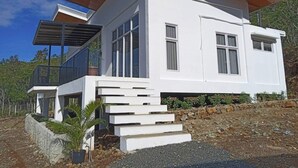 A modern two-story house with a white exterior, wooden roof, and a stone retaining wall. - Fight Club Philippines (Puerto Princesa)