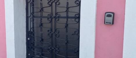 Una puerta con reja de hierro forjado, un marco blanco y una pared rosa con el número '1' encima.