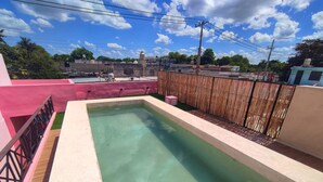 A rectangular swimming pool with a wooden deck and a pink wall on one side. - Apartamentos Casa Esquina (Mérida)