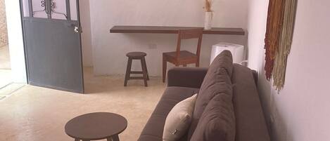 En stue med sofa, et rundt bord, en stol og et spiseområde med bord og stole.