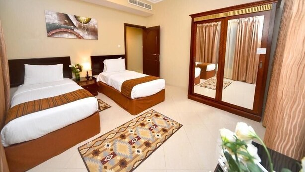 A hotel room with two beds, a large mirror, a painting on the wall, and a view of the outside through a window. - Two Bedroom Apartment Near Al Khan Beach By E R (الشارقة)