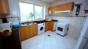 A compact kitchen with a washing machine, oven, and a window with a city view. - Two Bedroom Apartment Near Al Khan Beach By E R (الشارقة)