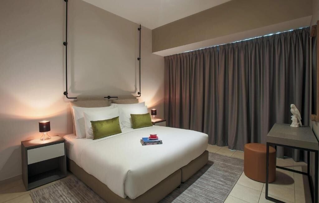Une chambre d’hôtel moderne avec un grand lit, des tables de chevet, un bureau et une fenêtre avec des rideaux.