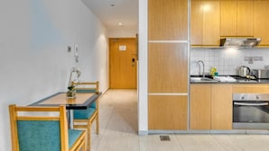A modern kitchen with wooden cabinets, a built-in oven, and a dining area with a table and chairs. - Studio Apartment Near Carrefour Tecom by E R (Dubai)