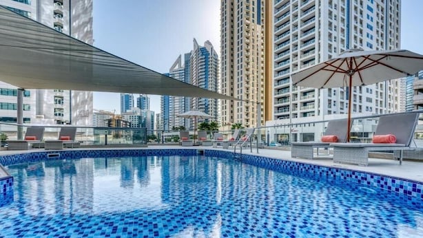 A rooftop pool with blue mosaic tiles, lounge chairs, and umbrellas. - Studio Apartment Near Carrefour Tecom by E R (Dubai)
