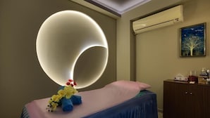 A massage room with a large illuminated circular light fixture, a massage table, and a cabinet with various items. - Studio Apartment Near Carrefour Tecom by E R (Dubai)