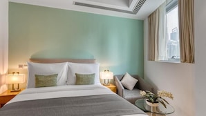 A hotel room with a bed, two bedside lamps, a grey sofa, a small round table with a plant, and a window with curtains. - Studio Apartment Near Carrefour Tecom by E R (Dubai)