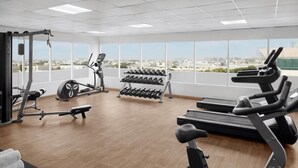 Academia com máquinas de cardio, halteres e um banco.