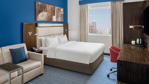 Quarto de hotel com uma cama grande, uma escrivaninha, uma cadeira, um sofá e um quadro na parede.