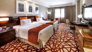 A hotel room with two beds, a desk, a TV, and artwork on the wall.