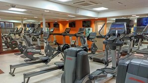 A gym with multiple treadmills and elliptical machines, mirrors on the walls, and exercise screens.