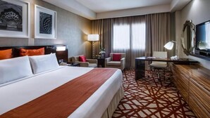 A hotel room with a large bed, a desk, a chair, a TV, and artwork on the walls.