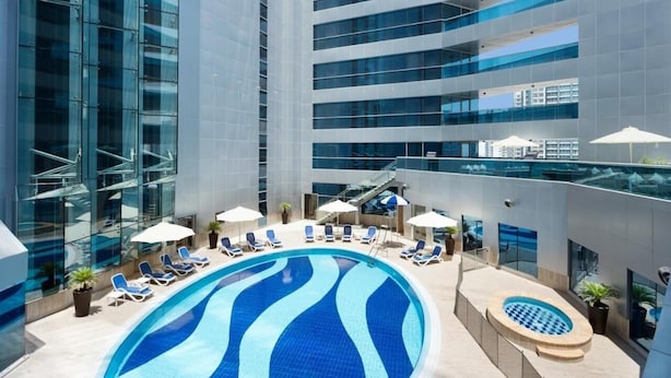 A modern hotel with a rooftop infinity pool, sun loungers, and a glass facade. - Standard Room In Business Bay By E R (Dubai)