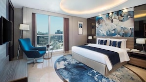 A modern hotel room with a large bed, a blue armchair, a flat-screen TV, and a city view. - Standard Room In Business Bay By E R (Dubai)