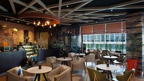 A modern café interior with exposed brick walls, a variety of seating options including round tables and chairs, and a large window providing natural light. - Standard Room In Business Bay By E R (Dubai)