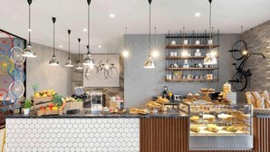 Un café moderne avec un comptoir recouvert de carreaux hexagonaux, des luminaires suspendus et une variété de produits de boulangerie et de pâtisserie présentés en évidence.