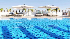 Une piscine dont le fond est recouvert de carreaux bleus, avec des chaises longues et des parasols.
