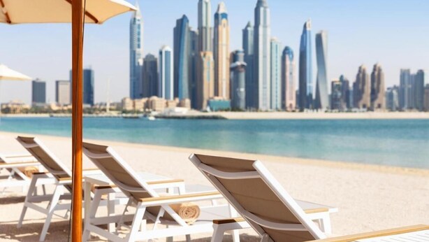Une vue sur la plage, avec des chaises longues et, en arrière-plan, le profil de la ville.