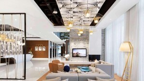 Un hall d’hôtel moderne, doté d’un canapé d’angle, d’un téléviseur à écran plat et d’un plafond décoratif.